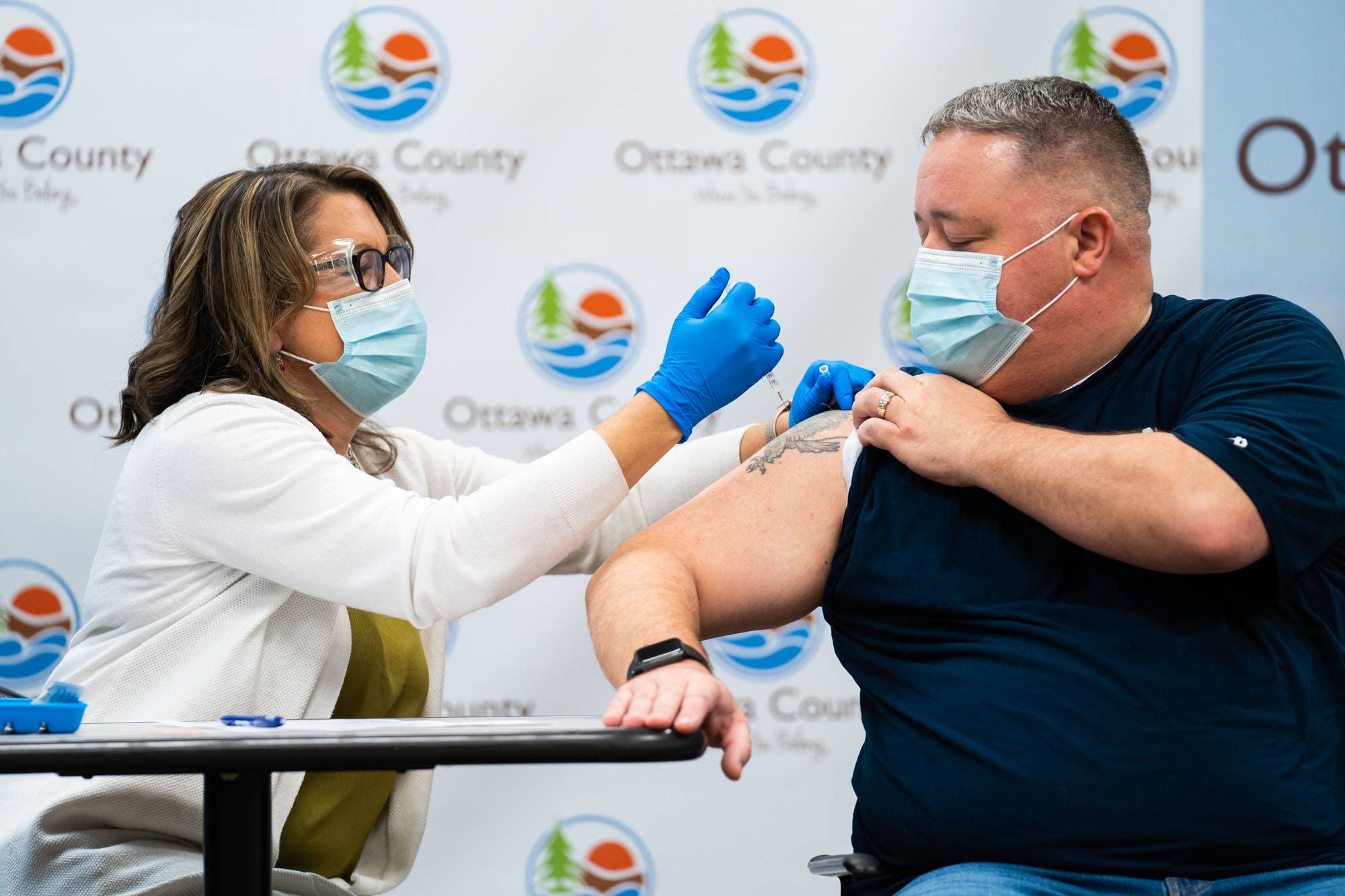 A health department worker gives a COVID-19 vaccine shot to a man with his sleeve rolled up.
